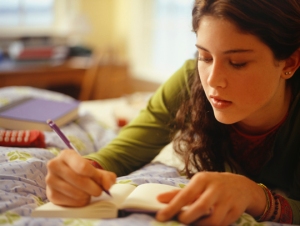 Teenage girl (16-17) lying on bed, writing, close-up